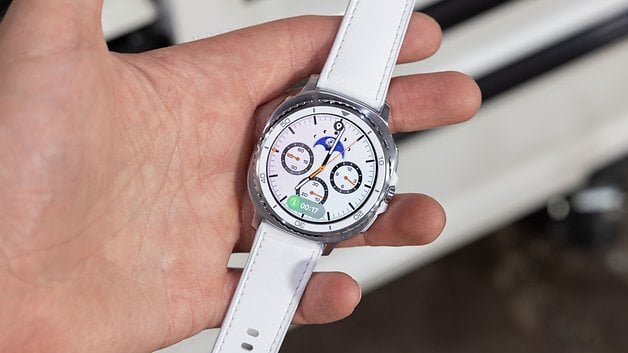Eine Person hält eine Samsung Galaxy Watch 8 Classic mit einem weißen Armband, die verschiedene Ziffernblätter zeigt.