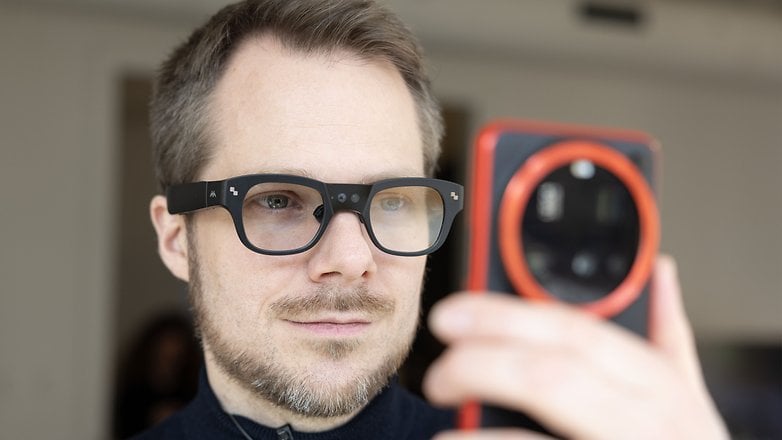 Ein Mann trägt eine smarte Brille und schaut auf die Kamera eines Smartphones.