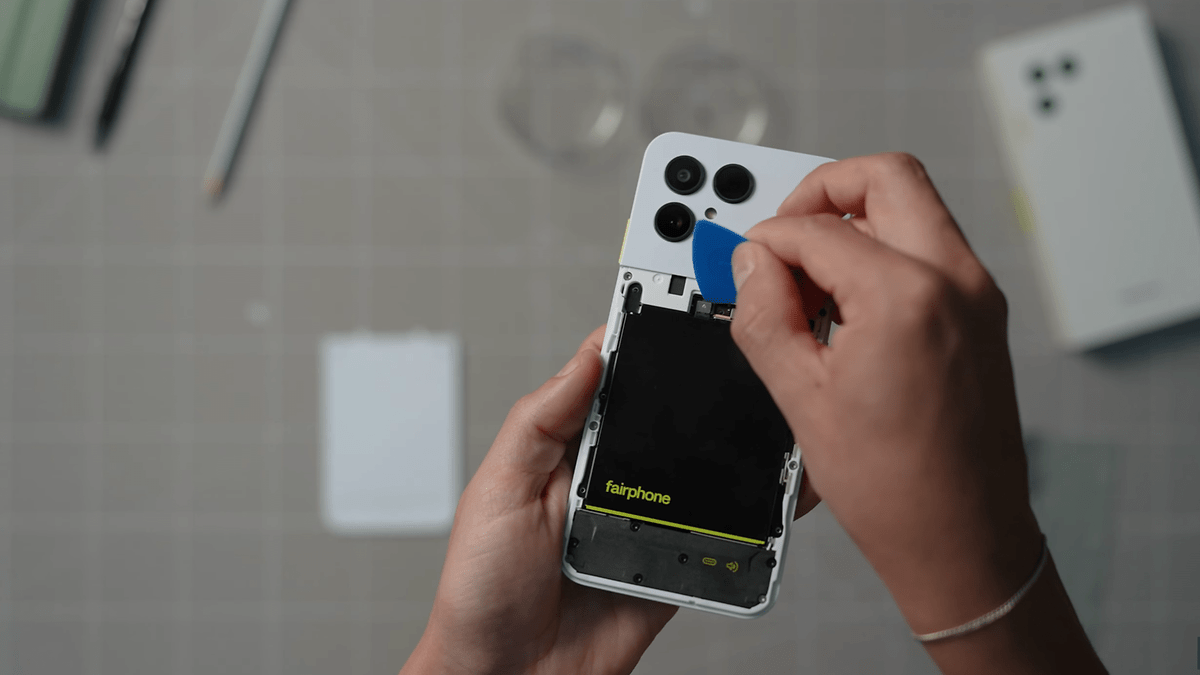 Une personne utilise un outil pour ouvrir l'arrière d'un smartphone Fairphone 6, révélant la batterie à l'intérieur.