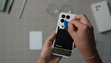 Eine Person verwendet ein Werkzeug, um die Rückseite eines Fairphone 6-Smartphones zu öffnen und die Batterie sichtbar zu machen.