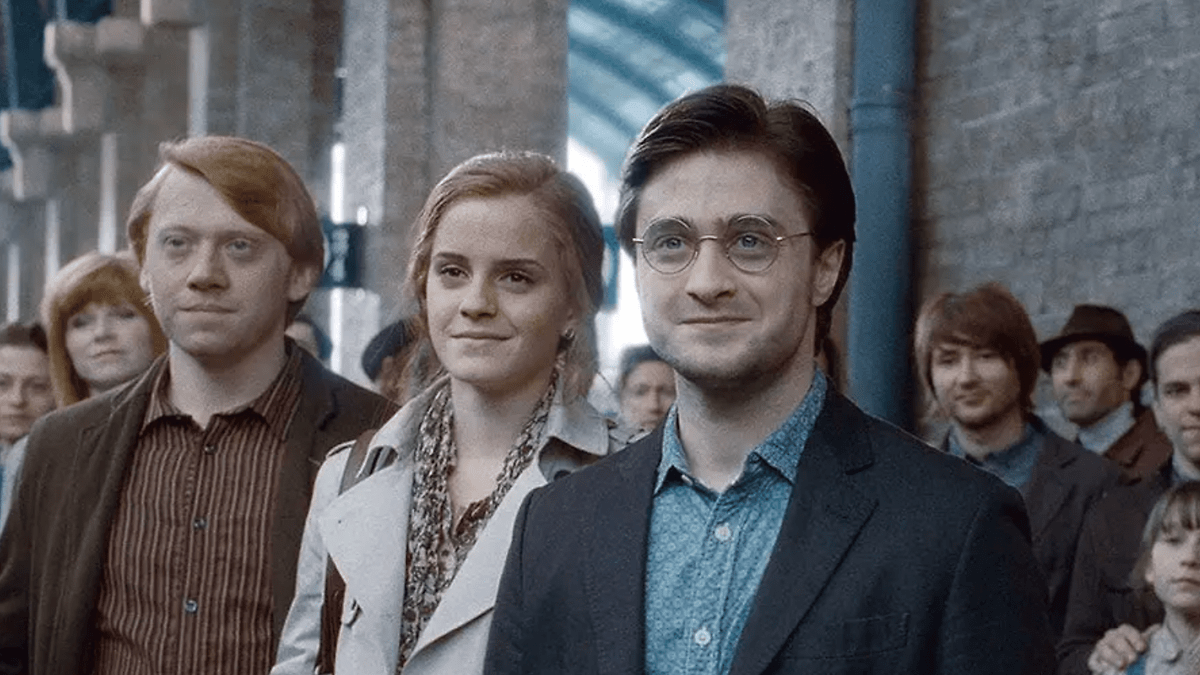 Trois amis se tiennent ensemble dans une gare bondée, souriant à l'objectif.