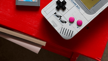 Eine LEGO-Nachbildung eines Game Boy auf einem roten Tisch mit einer Spielkarte daneben.