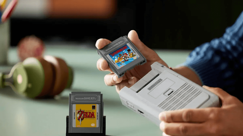 Eine Person hält eine Game Boy-Cartridge mit der Bezeichnung 'Super Mario' über einer Game Boy-Konsole mit der Cartridge 'Zelda'. Eine Person hält eine Game Boy-Cartridge mit der Bezeichnung 'Super Mario' über einer Game Boy-Konsole mit der Cartridge 'Zelda'.