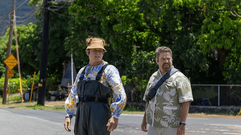 Two men stand on a road, one wearing a fishing outfit and a visor, the other in a Hawaiian shirt. Two men stand on a road, one wearing a fishing outfit and a visor, the other in a Hawaiian shirt.