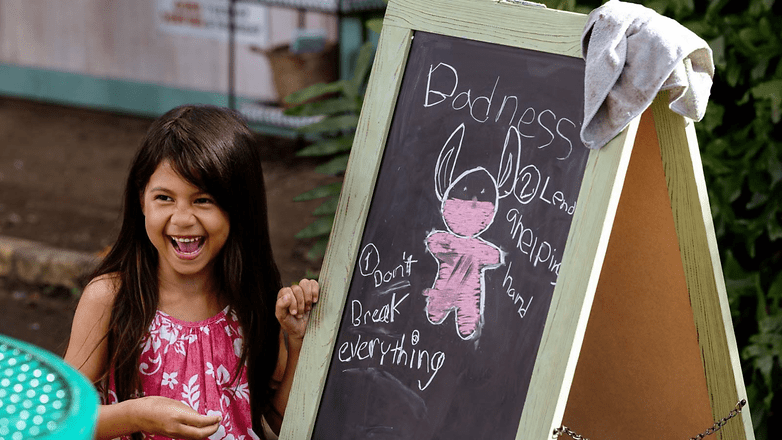 A girl smiles in front of a chalkboard with 'Badness' and a drawing of Stitch. A girl smiles in front of a chalkboard with 'Badness' and a drawing of Stitch.