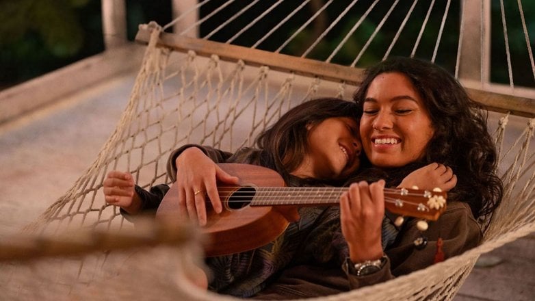 Two people relaxing in a hammock; one plays a ukulele while the other leans affectionately against them. Two people relaxing in a hammock; one plays a ukulele while the other leans affectionately against them.