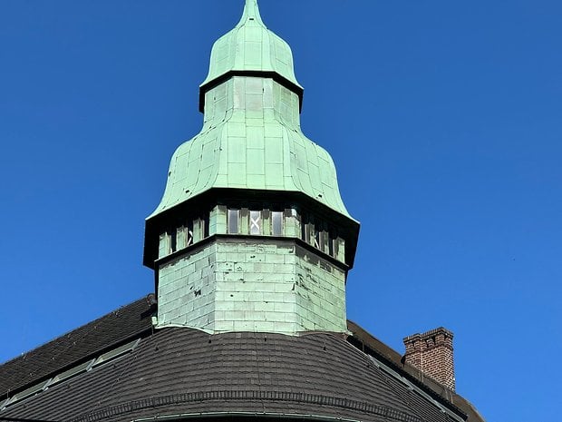 Photo prise avec l'iPhone 15 Pro Max de jour d'un bâtiment à un carrefour avec une tourelle au toit en taule de couleur vert-de-gris