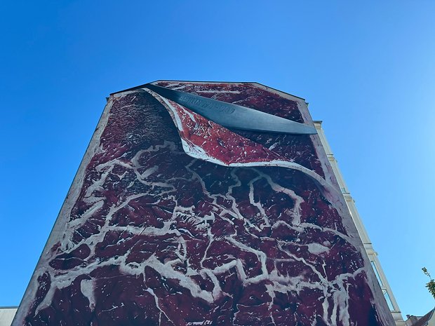 Photo prise avec l'iPhone 15 Pro Max de jour d'un bâtiment assez élevé avec un graffiti représentant un couteau qui tranche une pièce de viande