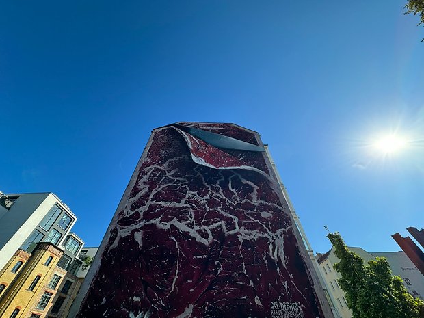 Photo prise avec l'iPhone 15 Pro Max de jour d'un bâtiment assez élevé avec un graffiti représentant un couteau qui tranche une pièce de viande