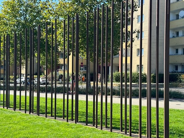 Photo prise avec l'iPhone 15 Pro Max de jour d'une portion de l'ex-mur de Berlin avec des pilliers en fer placés le long du tracé avec un parc d'un côté et une rue de l'autre