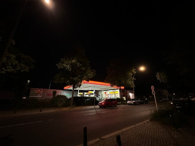 Photo prise avec l'iPhone 15 Pro Max de nuit d'une station essence au bord de la route avec des éclairages rouges et jaunes