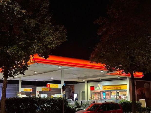 Photo prise avec l'iPhone 15 Pro Max de nuit d'une station essence au bord de la route avec des éclairages rouges et jaunes