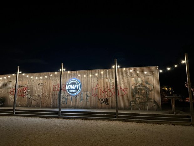 Photo prise avec l'iPhone 15 Pro Max de nuit de la devanture en bois d'un bar orné d'une pancarte circulaire et rétroéclairée