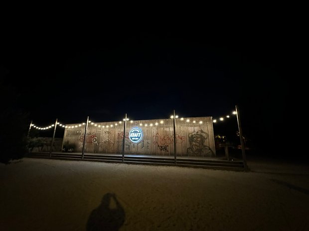 Photo prise avec l'iPhone 15 Pro Max de nuit de la devanture en bois d'un bar orné d'une pancarte circulaire et rétroéclairée
