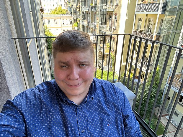 Selfie pris avec l'iPhone 15 Pro Max de jour avec Antoine portant une chemise bleue, assis sur un balcon