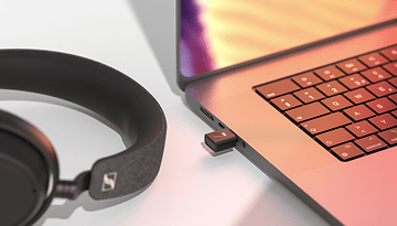 Adaptateur USB Bluetooth Sennheiser BTD 700 à côté des écouteurs et d'un ordinateur portable.