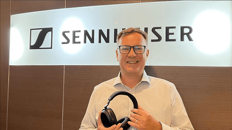 Christian Ern vor einem Sennheiser-Logo mit Kopfhörern in der Hand
