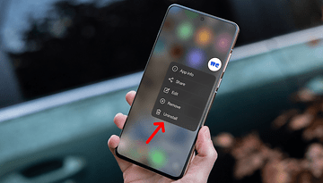 Une main tenant un smartphone affichant un menu avec des options, y compris 'Désinstaller' en surbrillance.