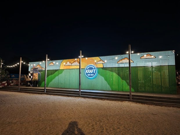 Une fresque colorée de collines et de nuages sur un bâtiment la nuit avec un logo bleu lisant 'KRAFT'.