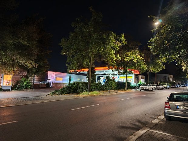 Une station-service la nuit avec des arbres le long de la rue et des voitures garées à proximité.