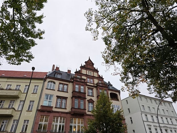 Bâtiments historiques avec une architecture ornée sous un ciel nuageux, encadrés par des arbres.