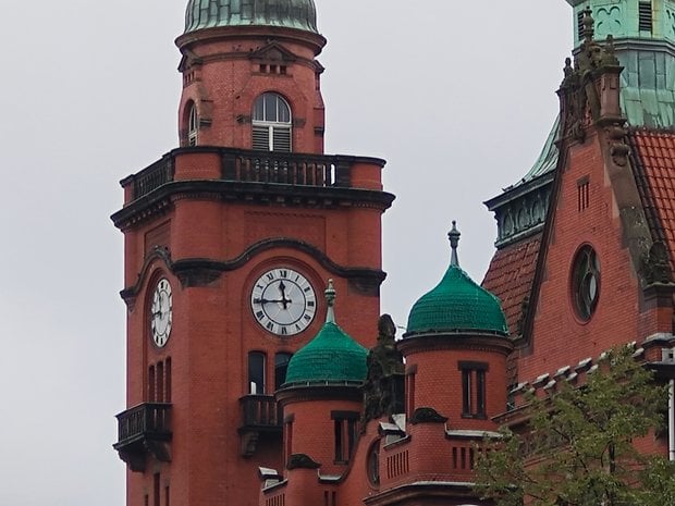 Un gros plan d'une tour de clocher en brique rouge avec des dômes verts sous un ciel nuageux.