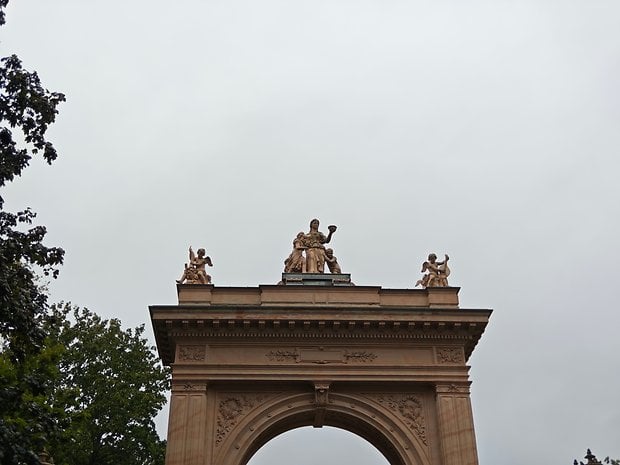 Une statue au sommet d'une arche, avec des figures sous un ciel nuageux.