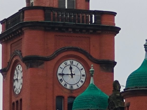 Gros plan d'une tour de l'horloge avec des chiffres romains sur un bâtiment en briques et des dômes verts.