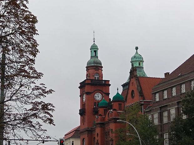 Bâtiment historique avec dômes verts et horloge par temps nuageux.