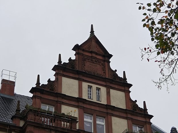 Détail architectural d'un toit en pignon avec un design orné et un ciel nuageux.