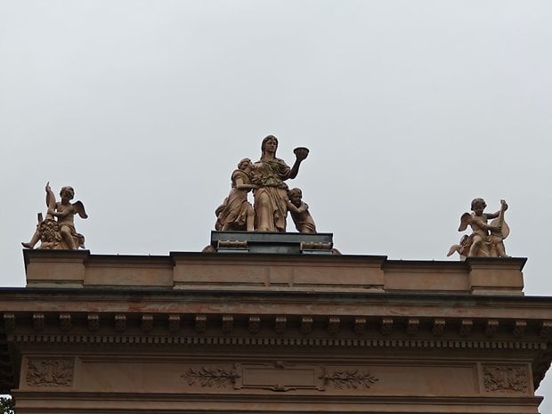 Statue au sommet d'un bâtiment avec une femme, des enfants et des chérubins sous un ciel gris.