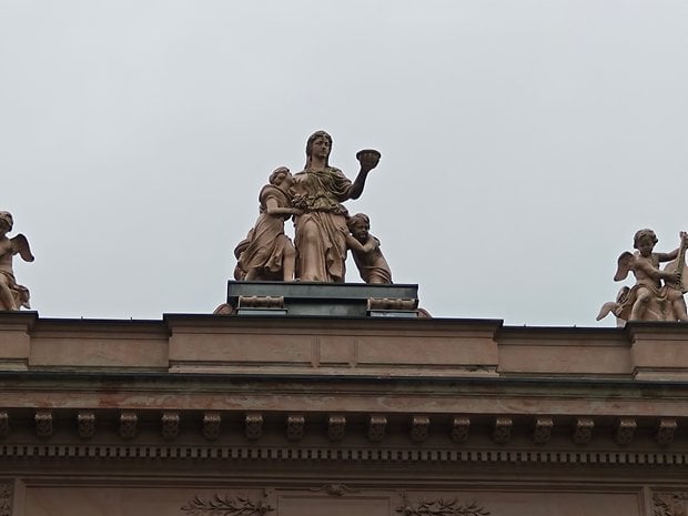 Statues sur le toit d'un bâtiment, avec une figure centrale entourée de deux enfants et de chérubins de chaque côté.