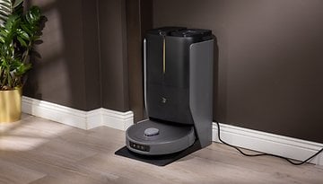 Ein Roboter-Staubsauger an seiner Ladestation gegen eine dunkle Wand.