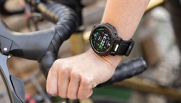 A hand wearing an Amazfit T-Rex Pro 3 smartwatch on a bike handlebar, displaying time and fitness data.