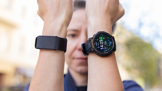 A person shows two wristbands, one is a black strap and the other is an Amazfit T-Rex Pro 3 watch displaying time and stats.