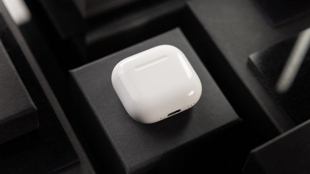 A pair of white Apple AirPods resting on a black surface.