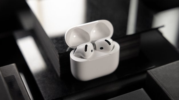 A pair of Apple AirPods in their charging case, placed on a dark surface.