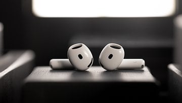 Two white Apple AirPods positioned on a dark surface with a soft background light.