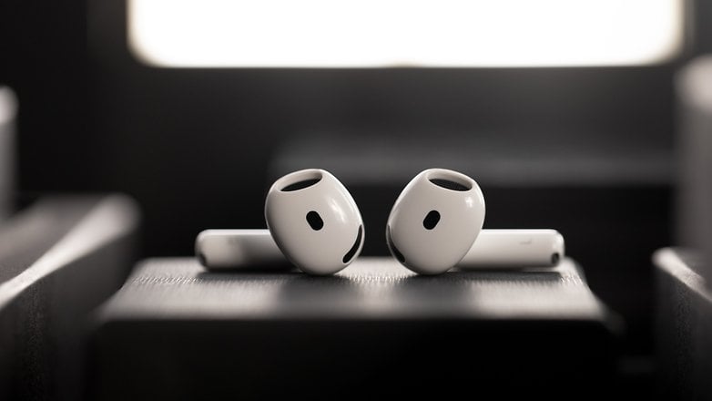 Zwei weiße Apple AirPods auf einer dunklen Oberfläche mit weichem Hintergrundlicht. Zwei weiße Apple AirPods auf einer dunklen Oberfläche mit weichem Hintergrundlicht.