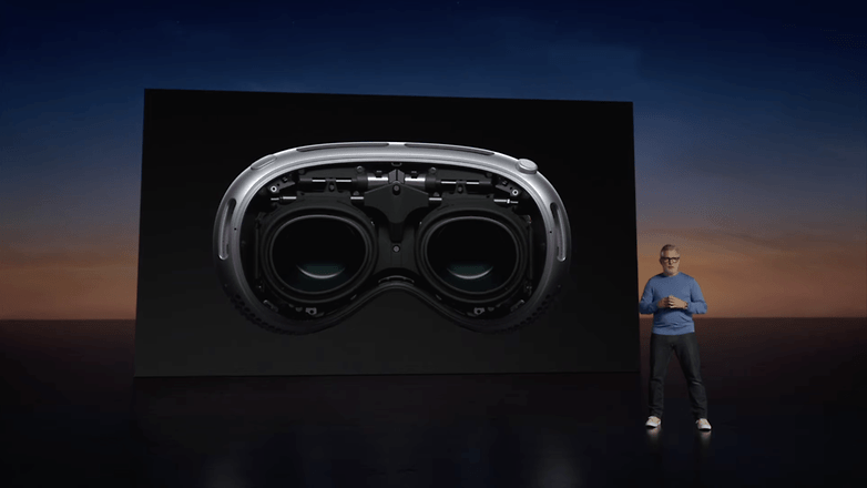 A speaker presents the Apple Vision Pro headset on stage, displayed on a large screen behind. A speaker presents the Apple Vision Pro headset on stage, displayed on a large screen behind.