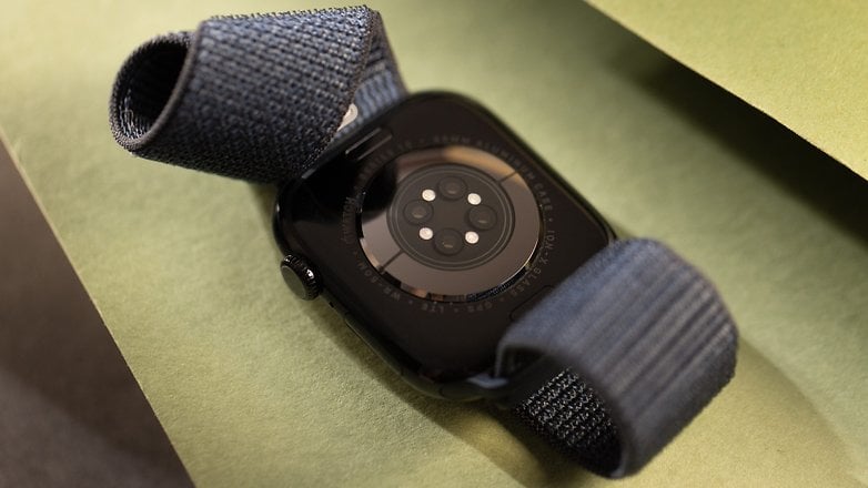 A black Apple Watch lying on green paper with a blue fabric strap.