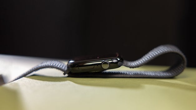 Vista lateral de um Apple Watch com uma pulseira cinza em uma superfície plana.