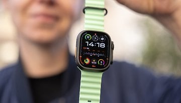 A close-up of an Apple Watch 3 Ultra on a green strap, displaying the time 14:18 and various fitness metrics.