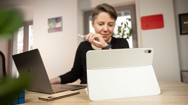 Uma mulher usando um Apple iPad 2022 branco com uma caneta enquanto está sentada em uma mesa com um laptop.