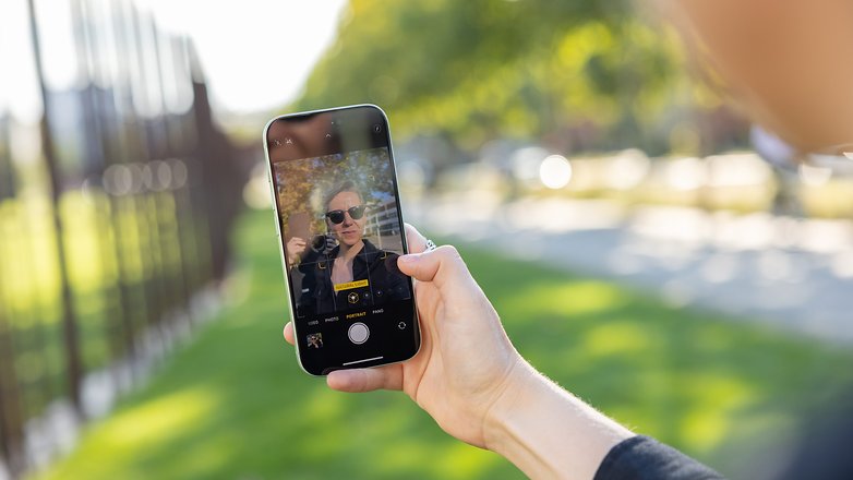 L'iPhone 15 vu de face tenu dans une main droite avec l'appareil photo ouvert en mode selfie et Camila visible à l'écran