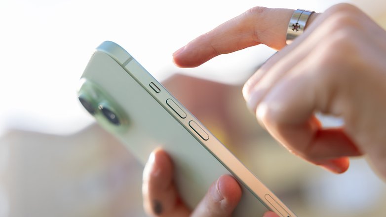 L'iPhone 15 vu de dos et de biais tenu dans une main avec l'index d'une autre main qui touche son écran