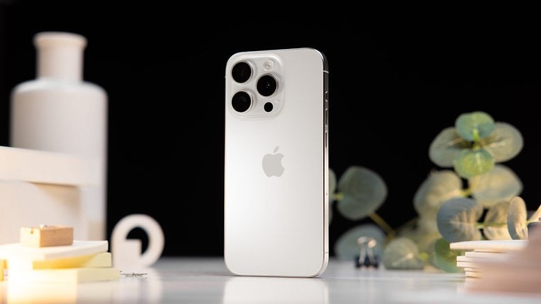 L'iPhone 15 Pro d'Apple posé verticalement sur une table et vu de dos dans son coloris blanc titane avec des décorations en arrière-plan