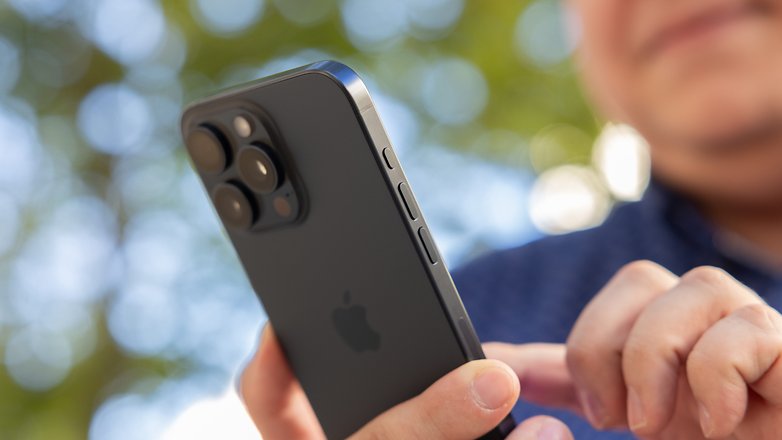 L'iPhone 15 Pro Max d'Apple vu de dos en plein soleil tenu dans une main droite