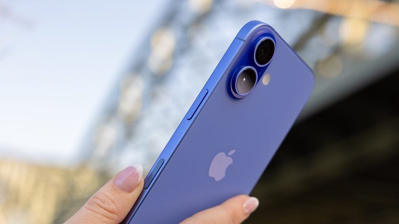 Une personne tenant un iPhone 16 bleu, mettant en avant sa caméra et ses boutons.