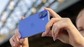 A person holding a blue iPhone 16 with dual cameras in a sunny outdoor setting.